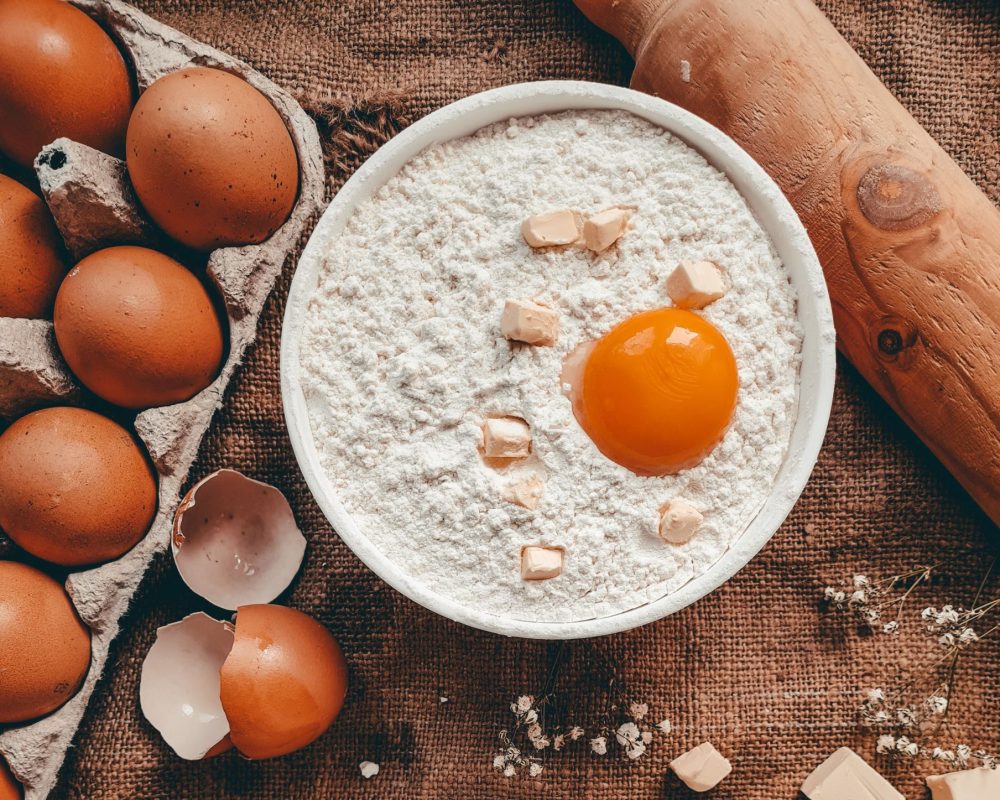 A cozy flat lay of baking ingredients, featuring eggs, flour, butter, and cottage cheese on a rustic surface.